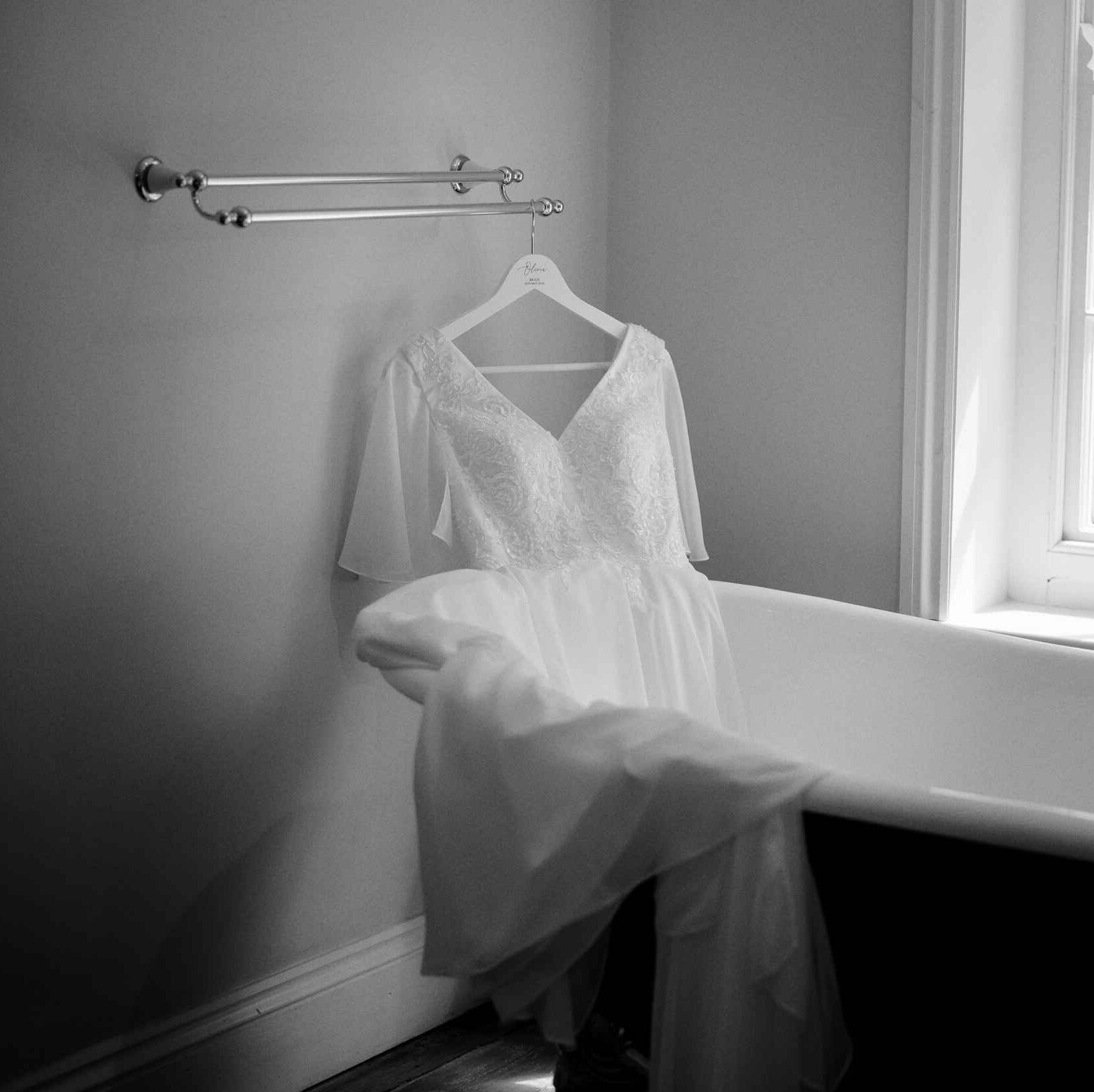Editorial B&W image of the brides dress draping over the bath.