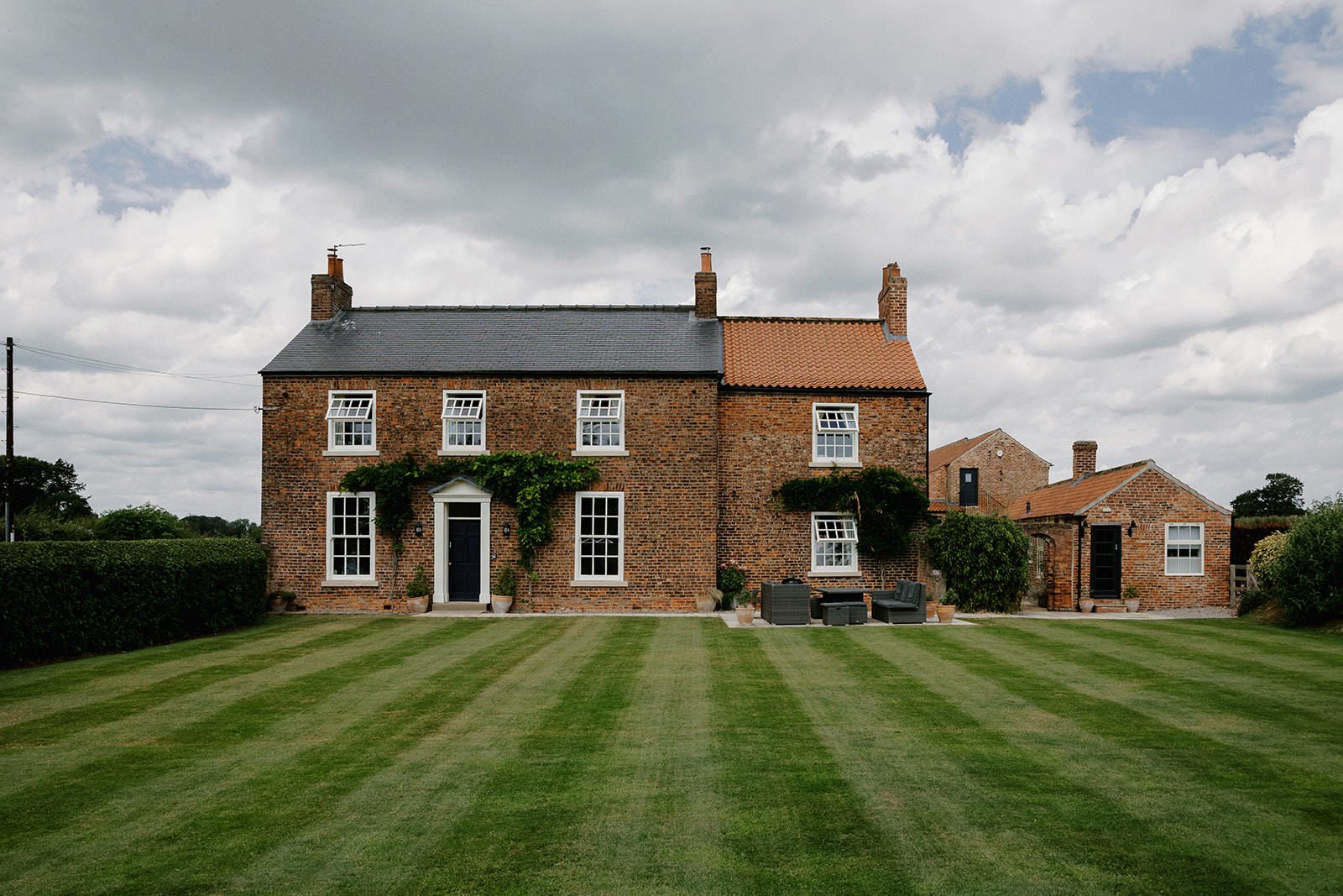 Georgian red-brick farmhouse with ivy and a striped lawn at Thirsk Lodge Barns