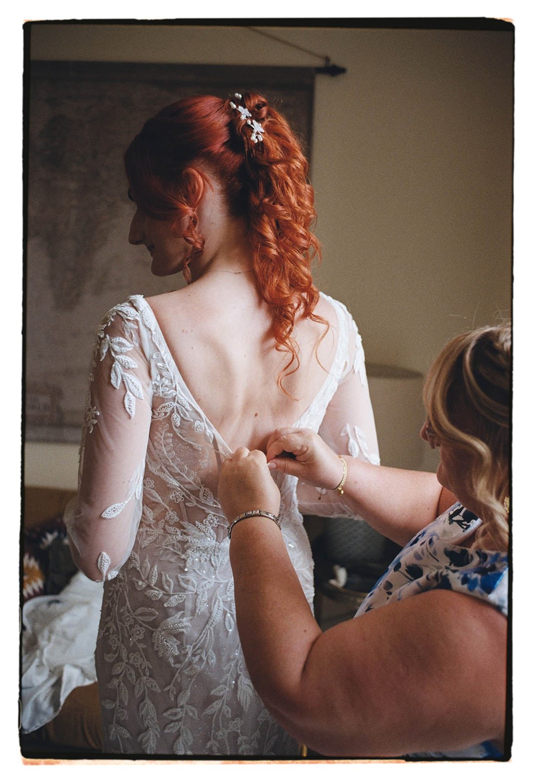 35mm film photo of the bride being buttoned into her lace gown with illusion mesh sleeves