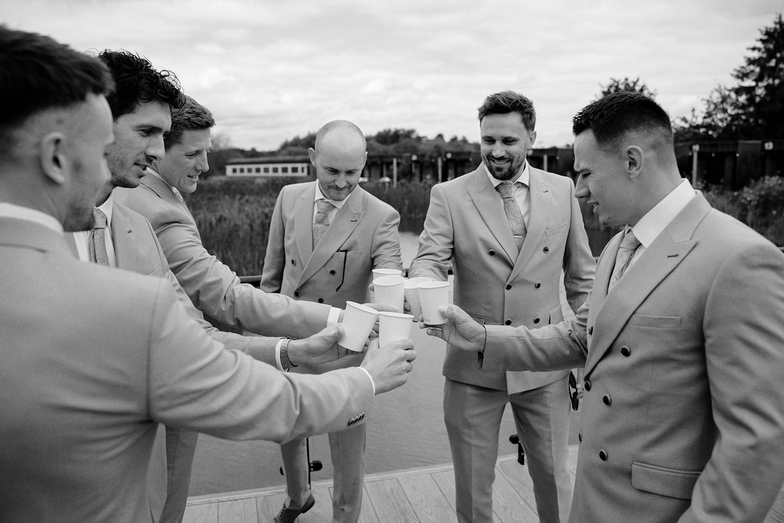Black and white photo of the groom and groomsmen in double-breasted suits raising a toast before the ceremony