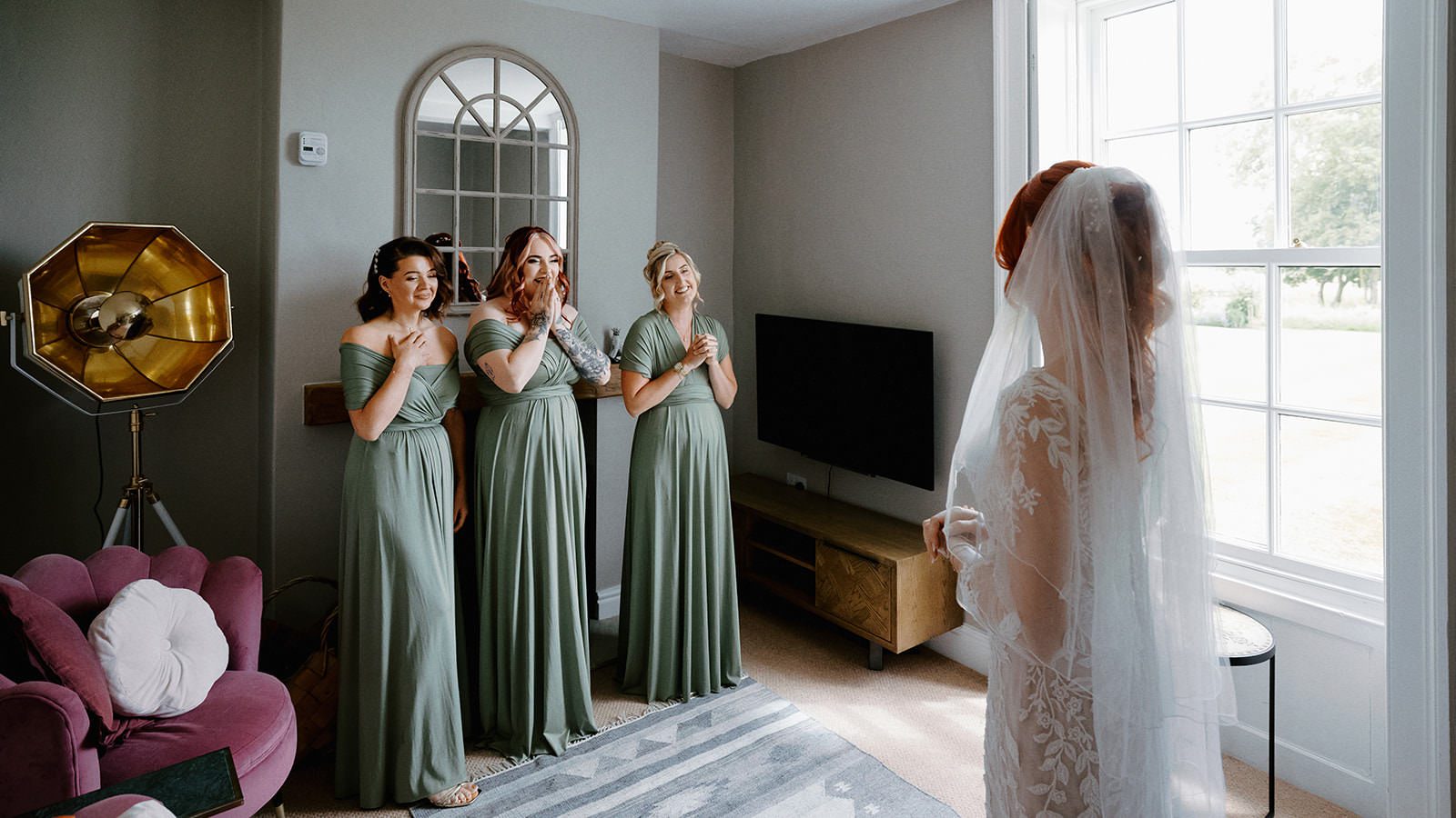 Three bridesmaids in sage green dresses with hands on their hearts at the bride's first look