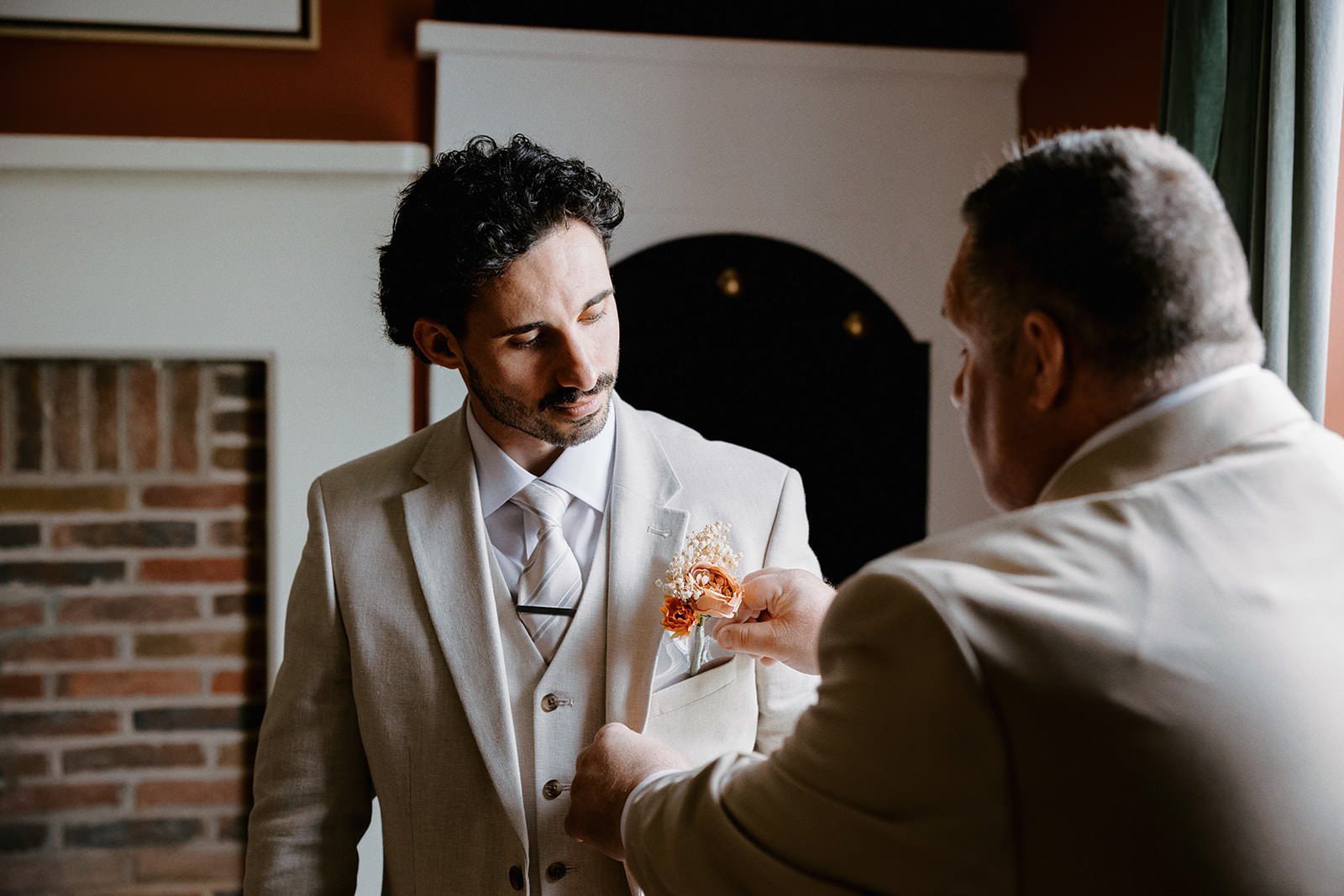 Groom having his dried flower buttonhole pinned to his stone three-piece suit