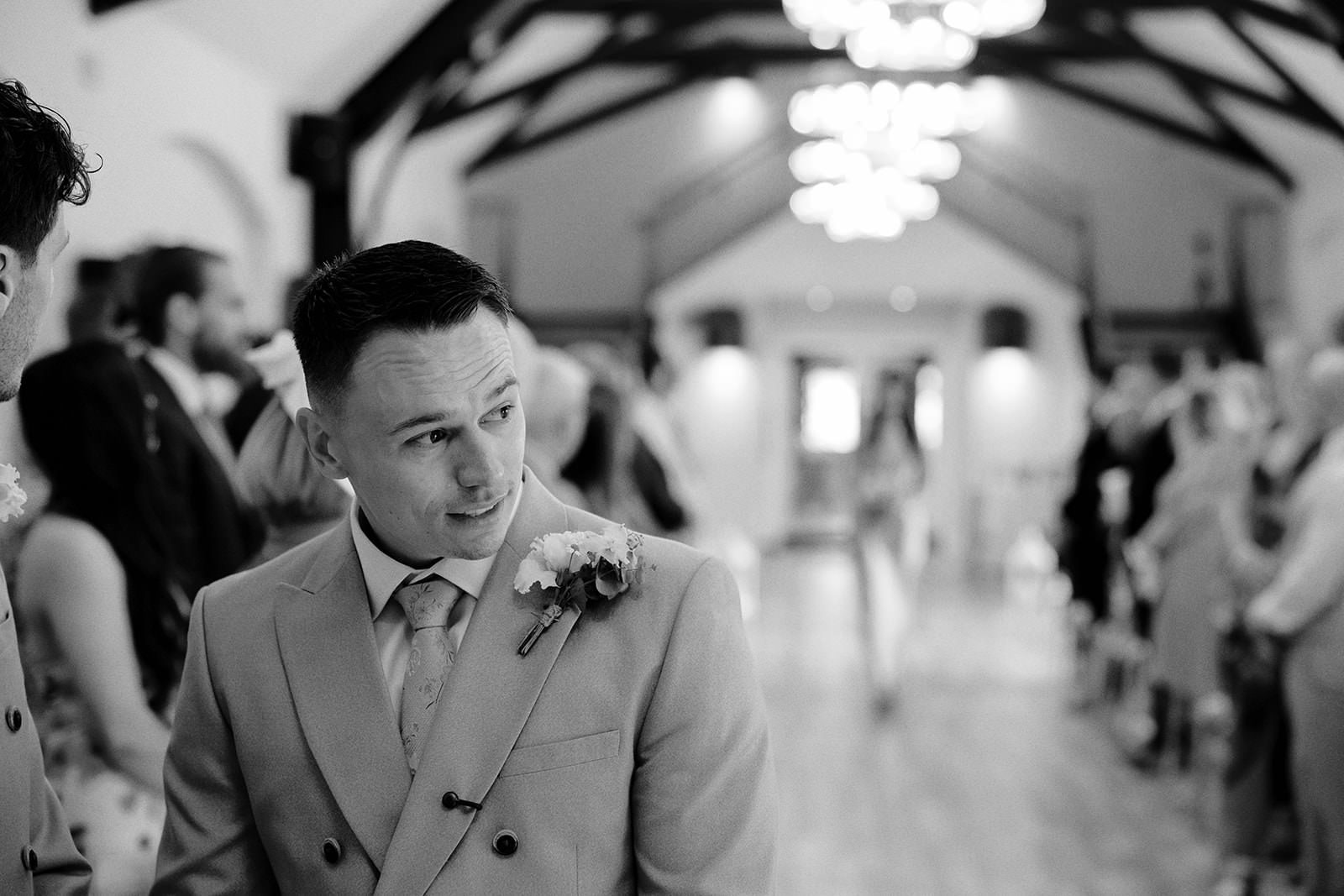 Black and white photo of the groom glancing back down the aisle as the bride is about to enter