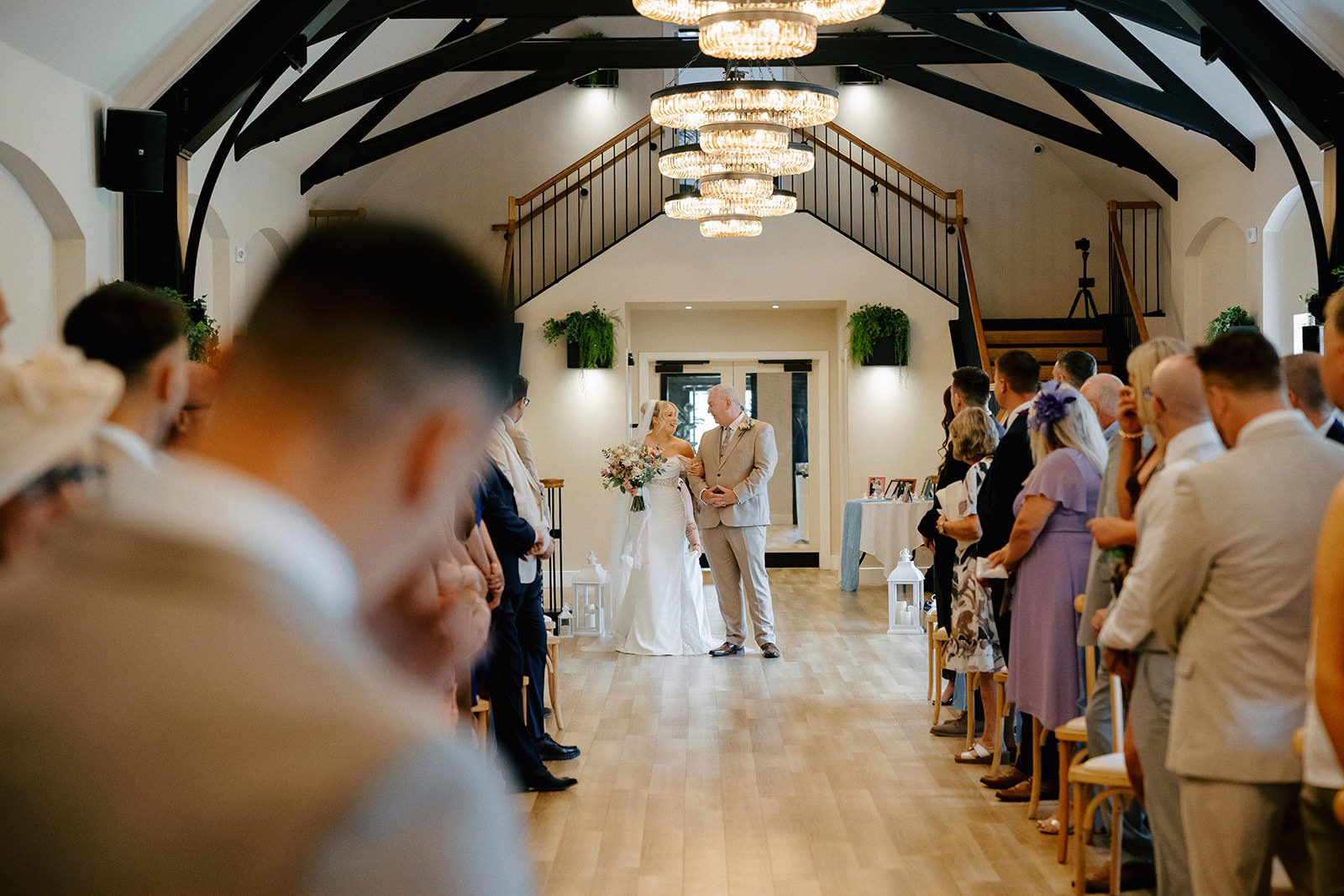 Bride and her father at the end of the aisle in the Whistle Barns ceremony barn with crystal chandeliers and black beams