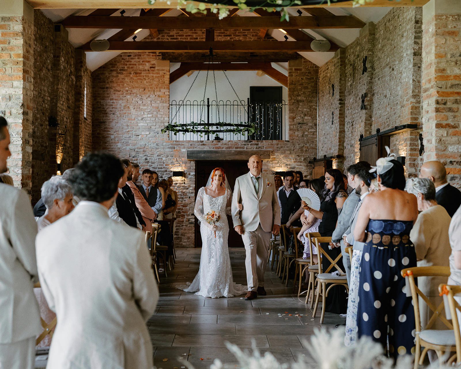 Bride walking down the aisle with her dad in the Thirsk Lodge Barns ceremony barn
