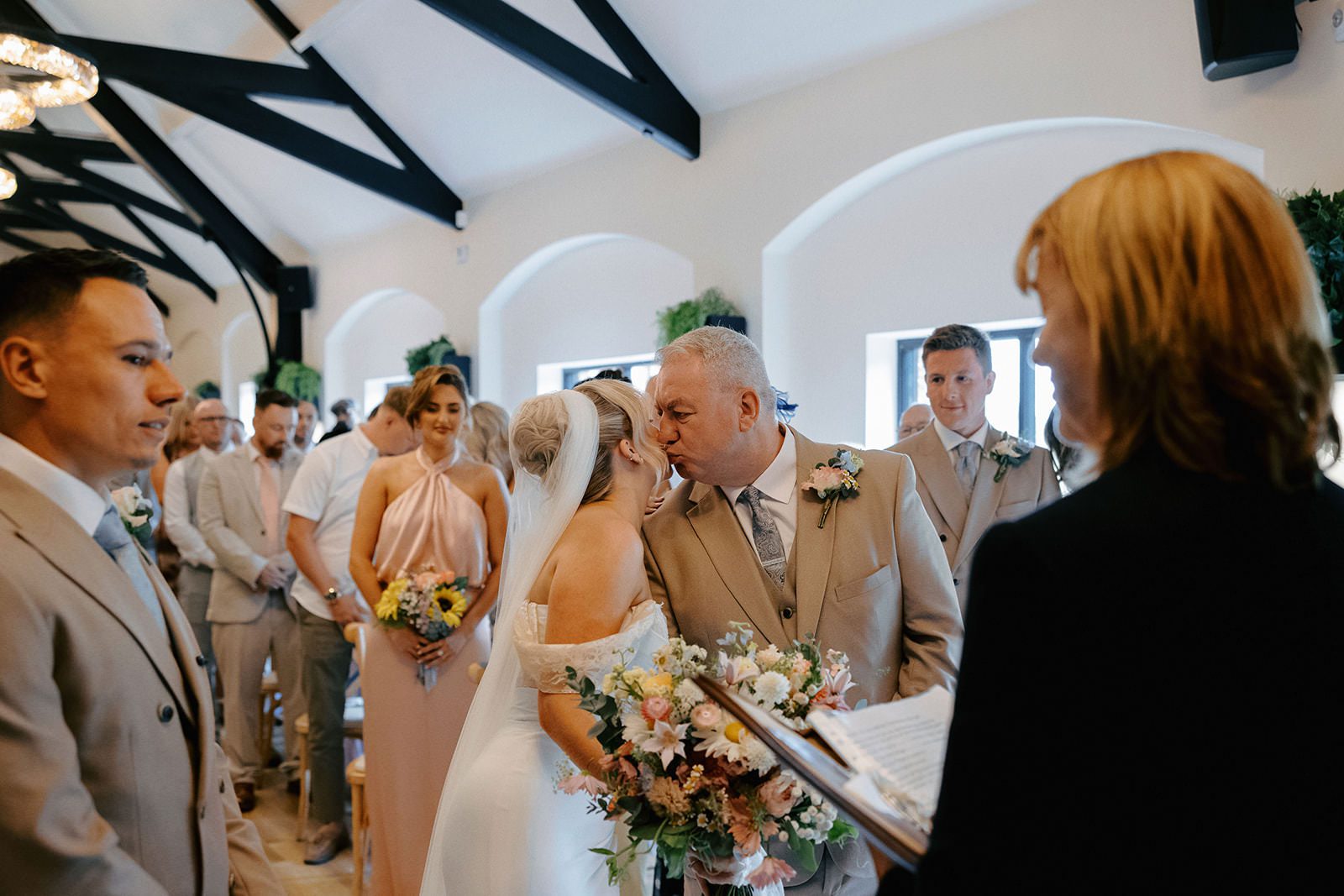 Father of the bride kissing his daughter on the cheek as he gives her away at the front of the ceremony barn