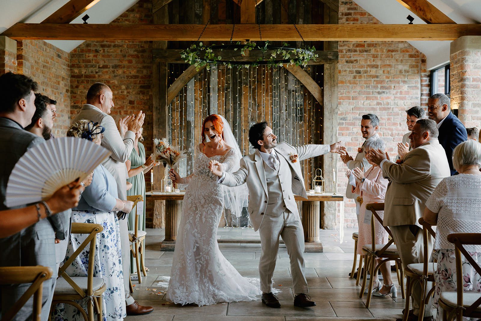 Bride and groom dancing back down the aisle as guests cheer and wave fans