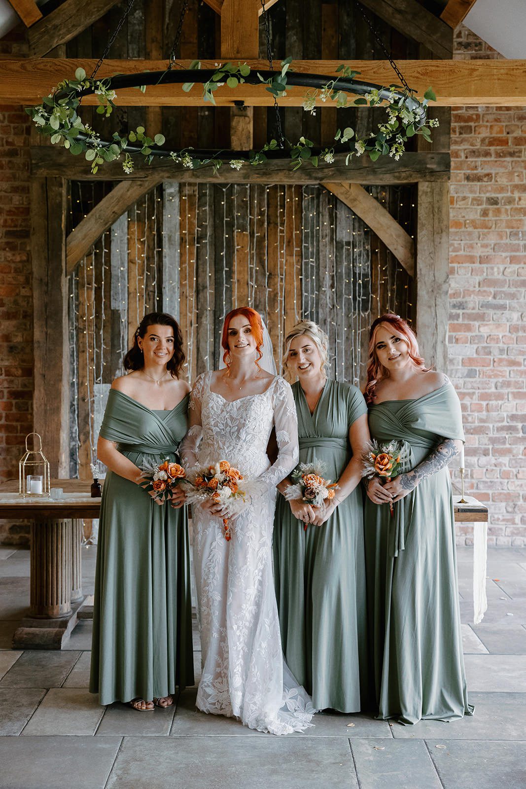 Bride with three bridesmaids in sage green holding copper and rose bouquets under the oak beams