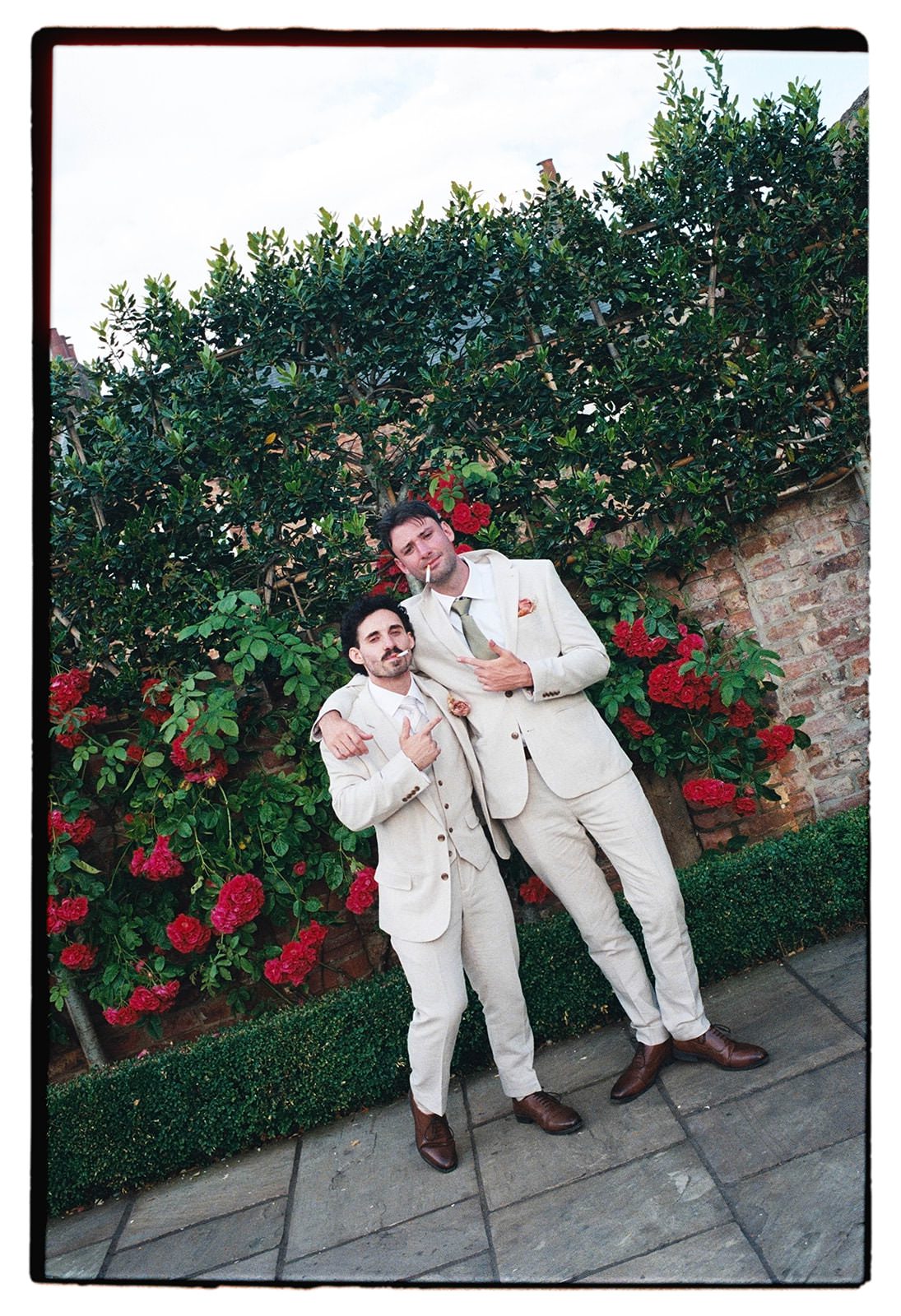 35mm film photo of two groomsmen striking a pose against a wall of red roses