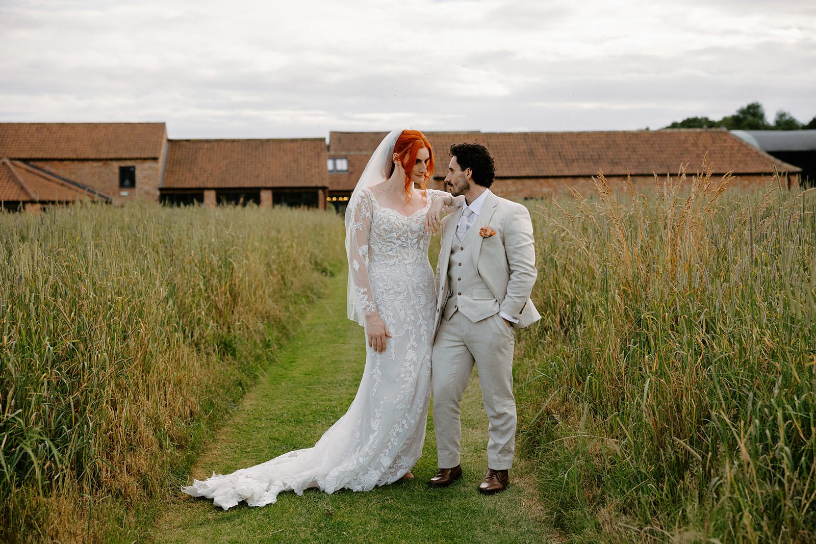 Bride and groom laughing together on a meadow path with Thirsk Lodge Barns behind them