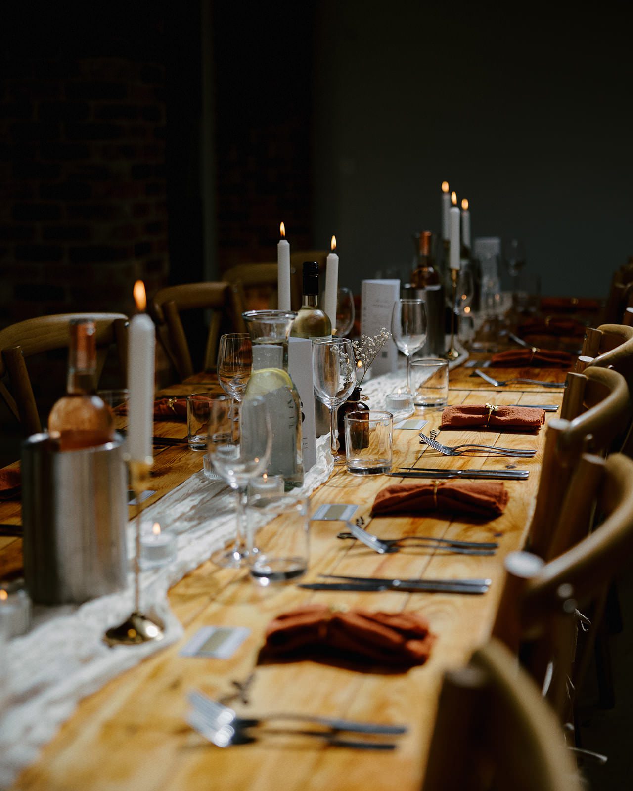Farmhouse oak tables set with copper napkins, white taper candles and a sheer runner in the reception barn