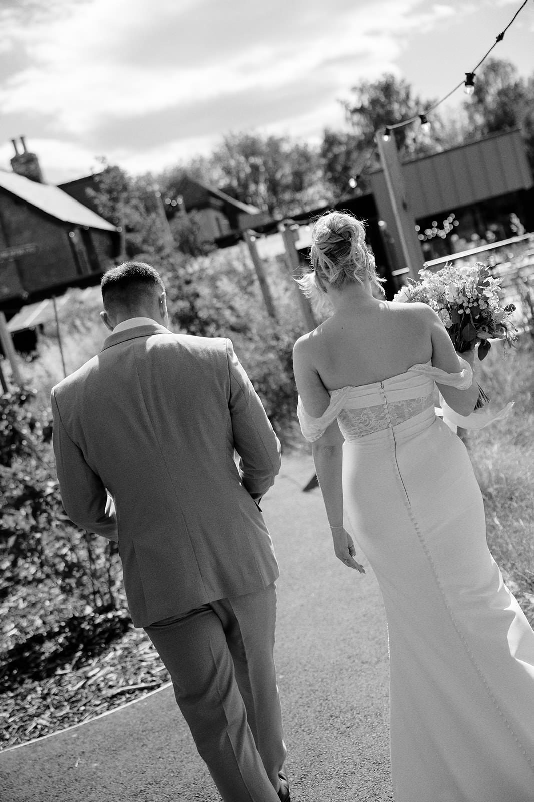 Black and white photo of the bride and groom walking away along a path through the gardens