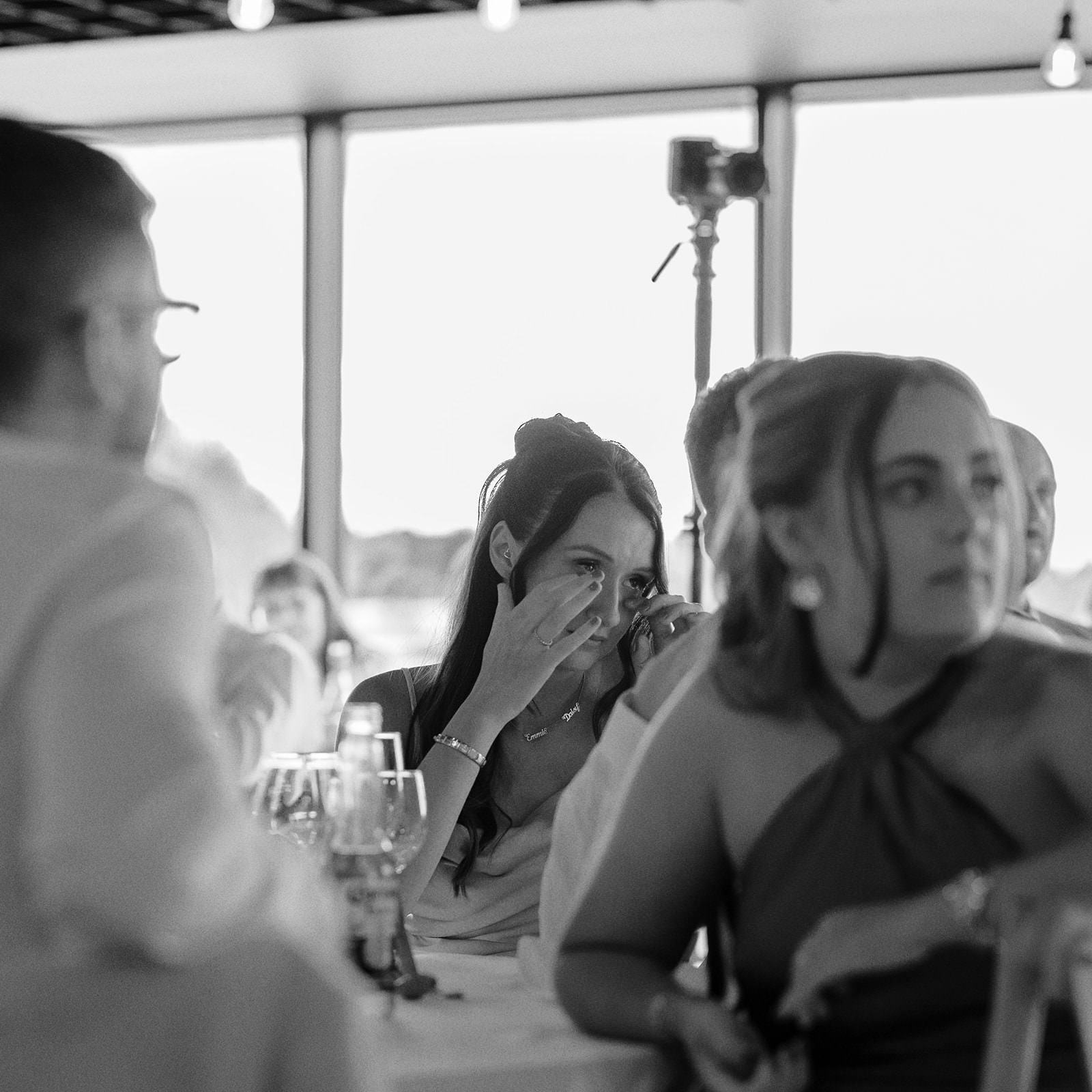 Black and white photo of a guest wiping a tear during the wedding speeches