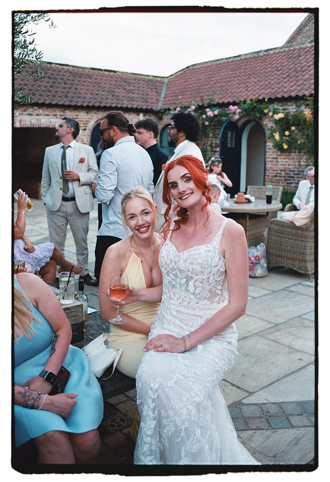 35mm film photo of the bride and a friend in yellow smiling with glasses of rosé in the courtyard