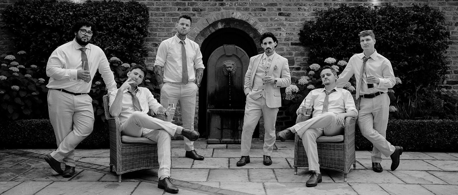 Black and white Vanity Fair style group photo of the groom and groomsmen lounging in the courtyard