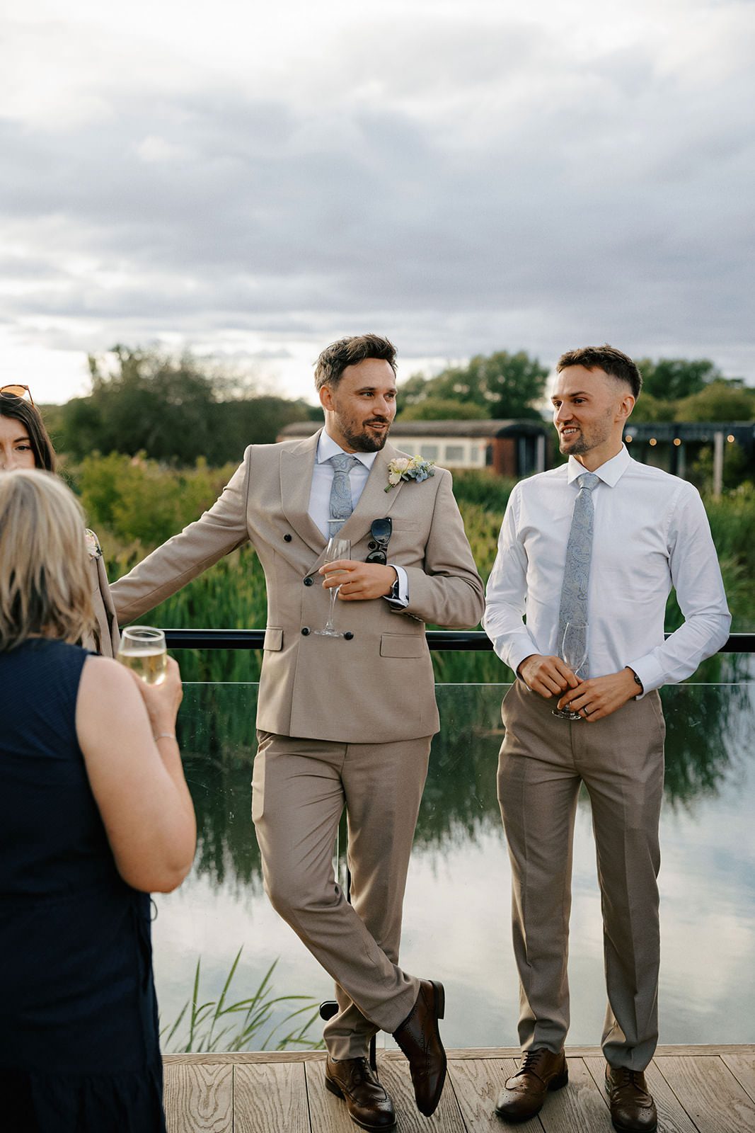 Two groomsmen chatting with drinks on the lakeside terrace in the evening