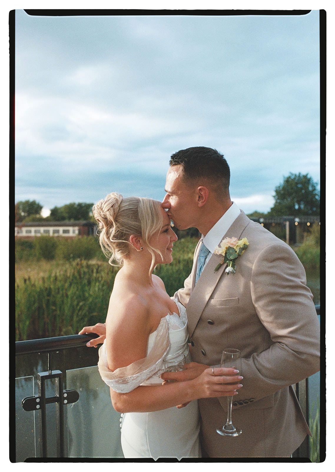 35mm film photo of the groom kissing the bride's forehead on the lakeside terrace
