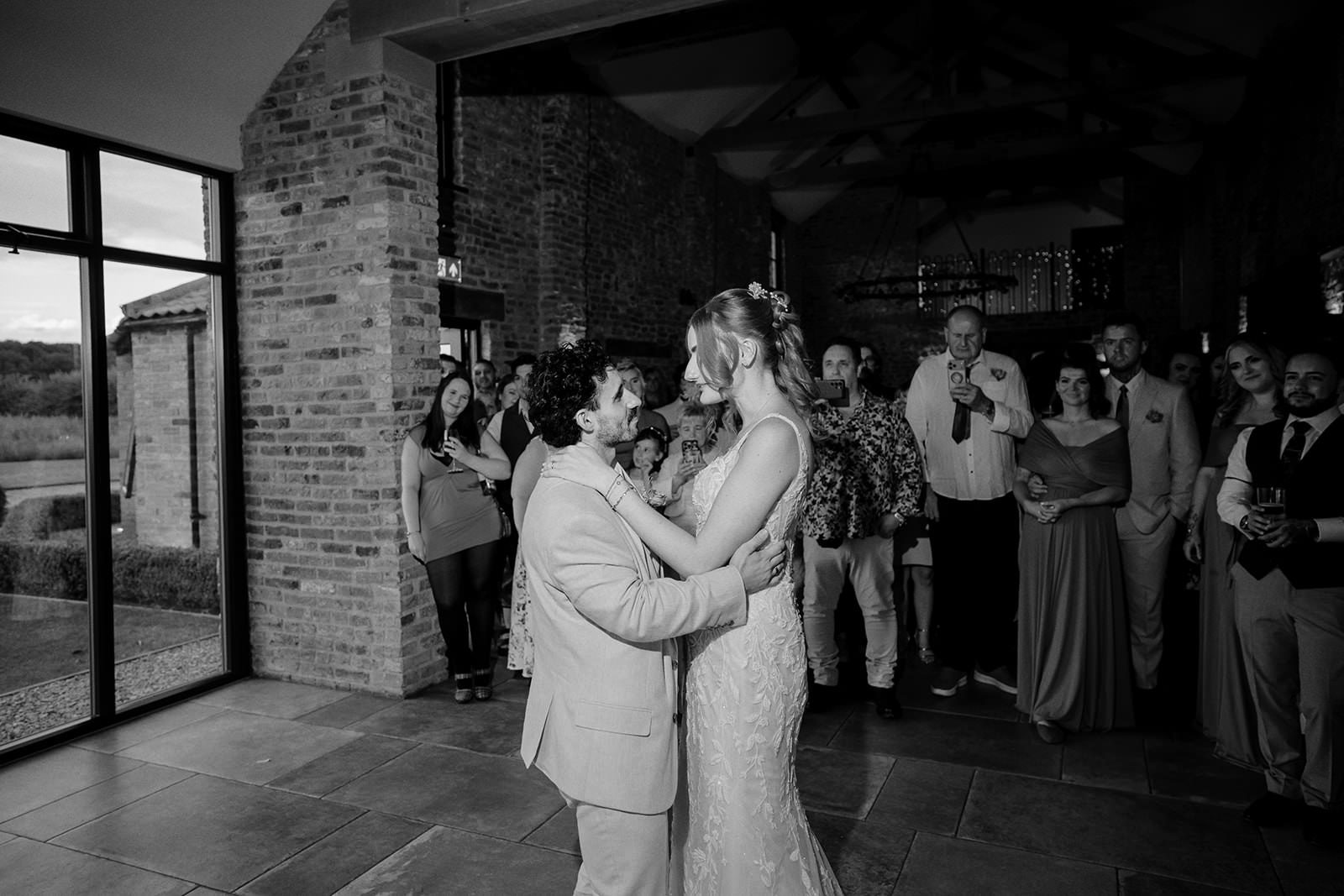 Black and white photo of the bride and groom's first dance in the Main Barn surrounded by guests