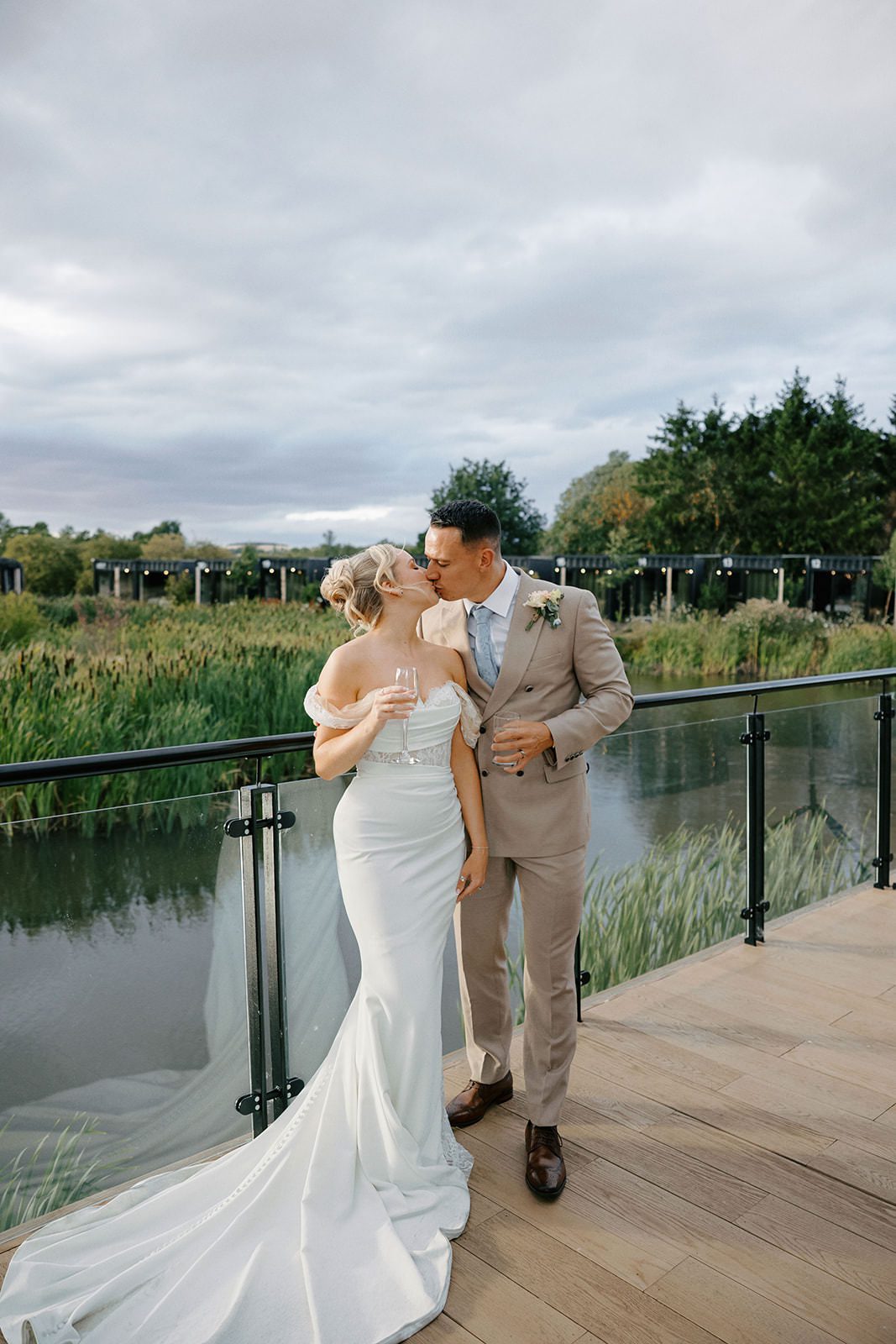 Bride and groom kissing on the lakeside terrace with her dress train spread across the decking