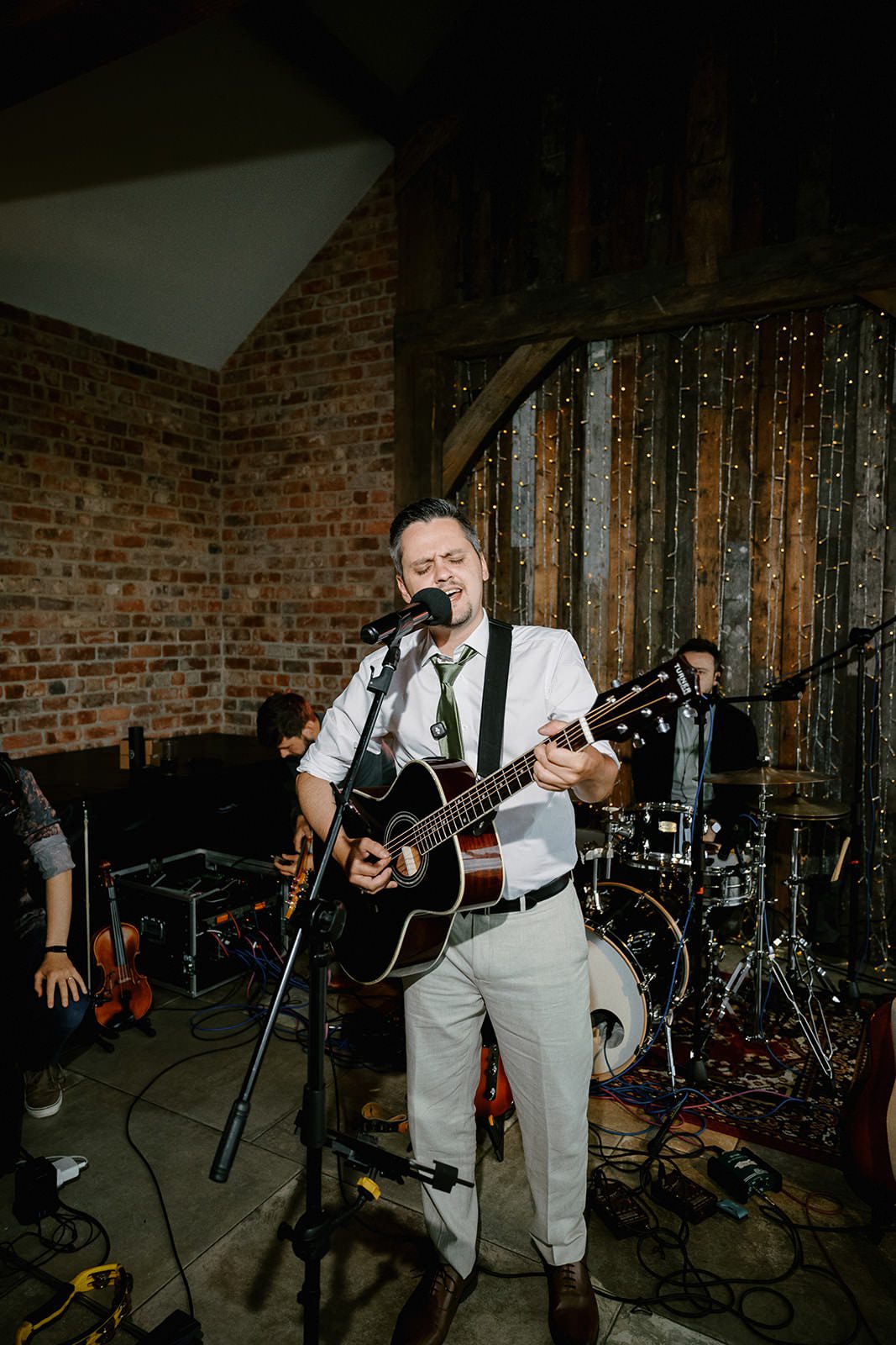 Band singer playing acoustic guitar under the fairy lights in the Main Barn