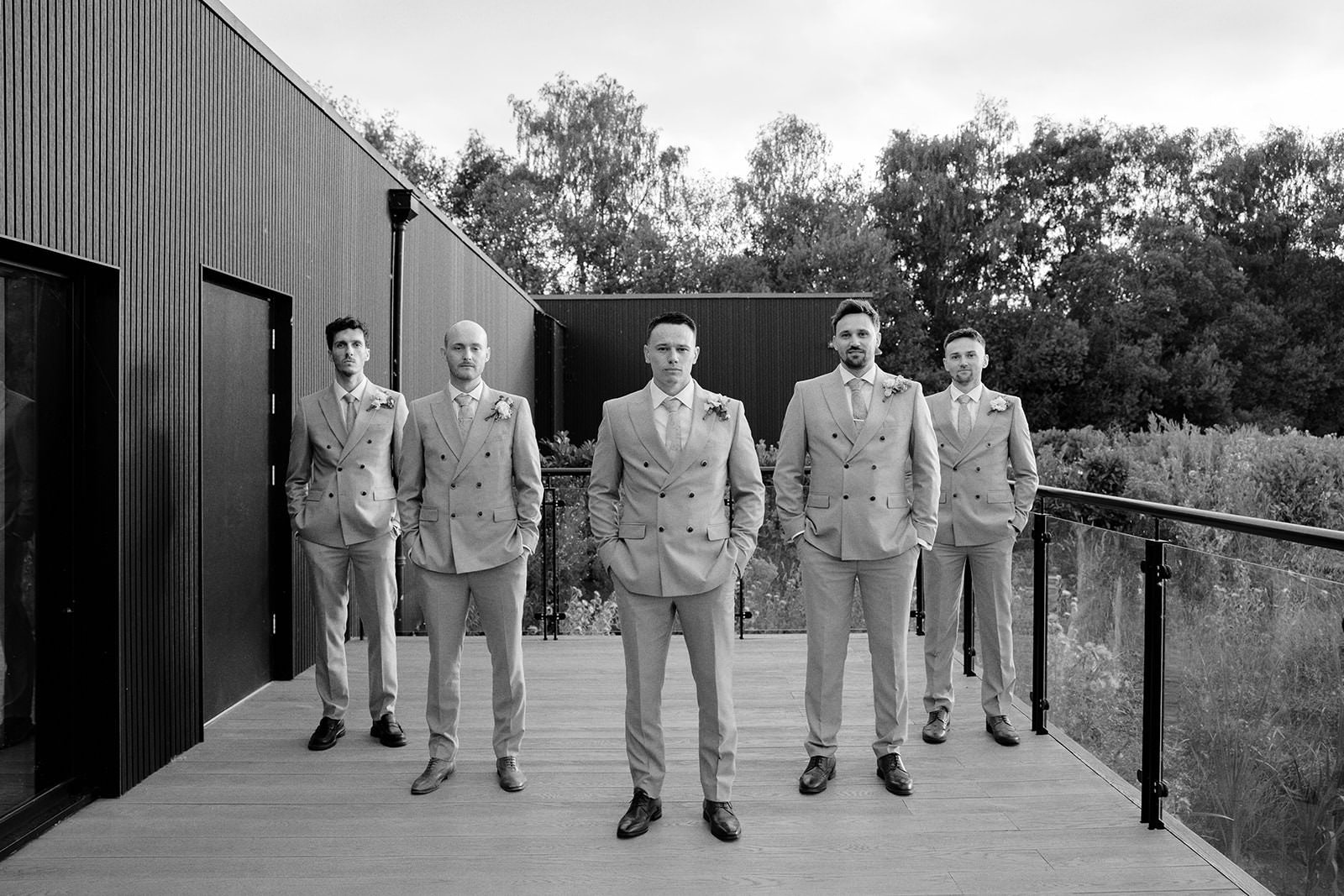 Black and white photo of the groom standing with his four groomsmen on the venue decking