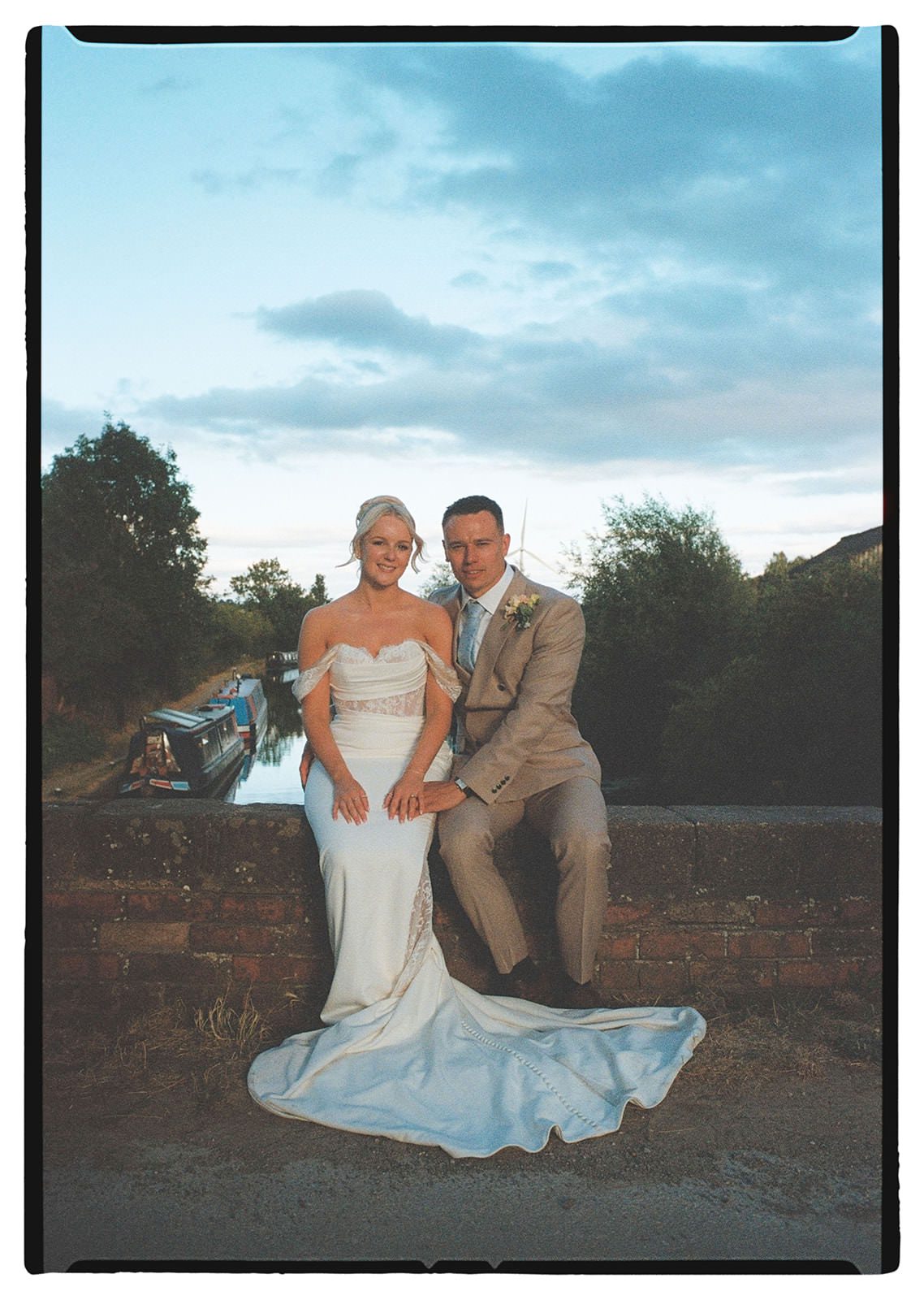 35mm film photo of the bride and groom on a canal bridge at sunset with narrowboats below