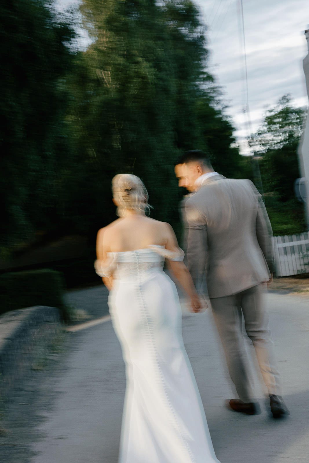 Motion blur photo of the bride and groom walking hand in hand down a tree-lined country lane