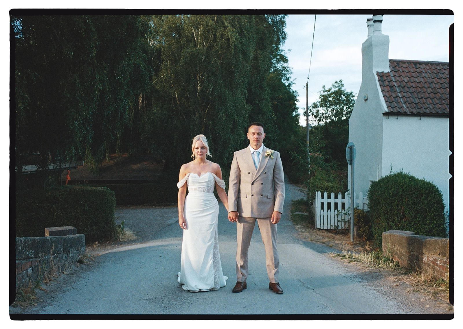 35mm film photo of the bride and groom holding hands on a country lane beside a whitewashed cottage