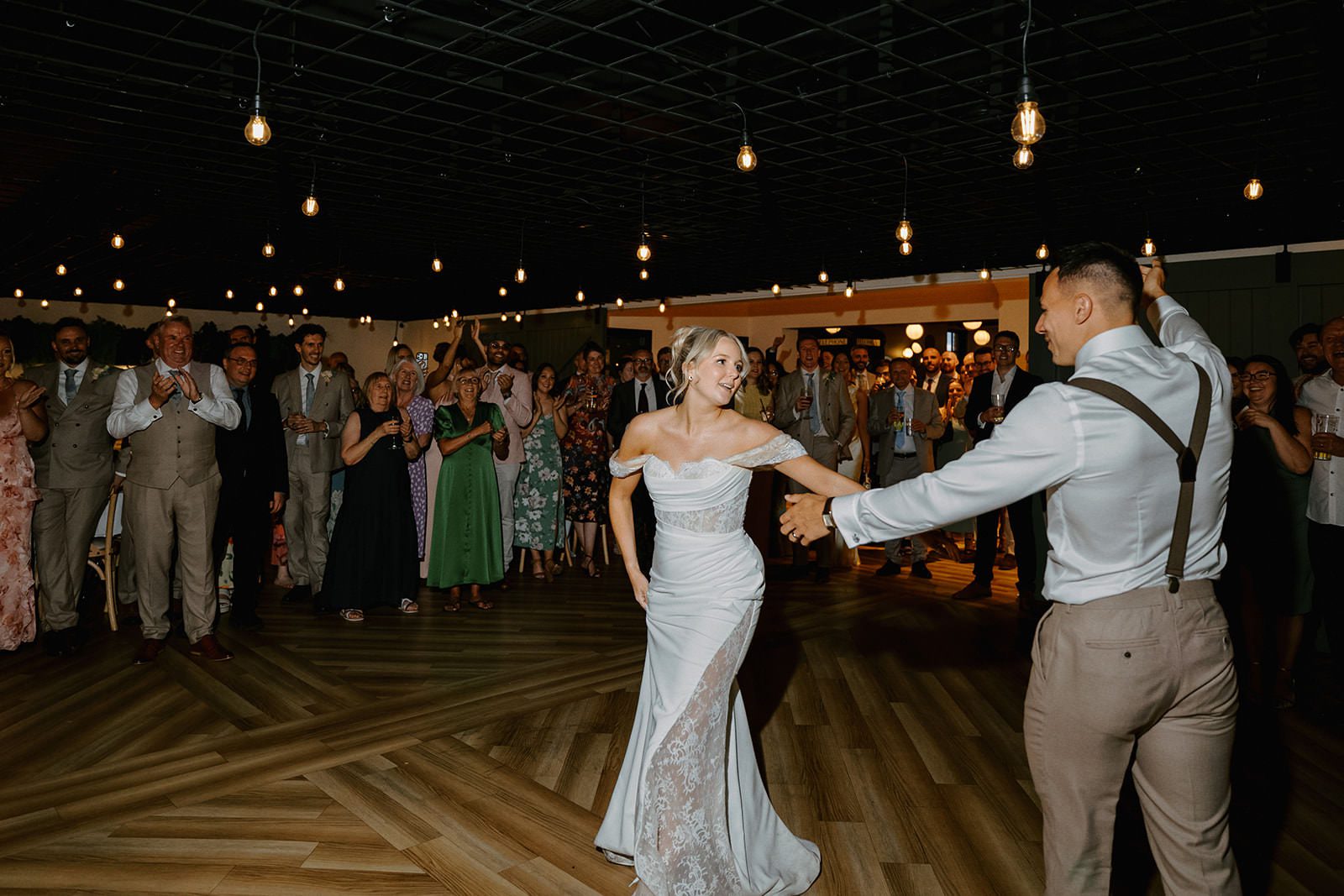Bride and groom starting their first dance surrounded by guests under festoon lights