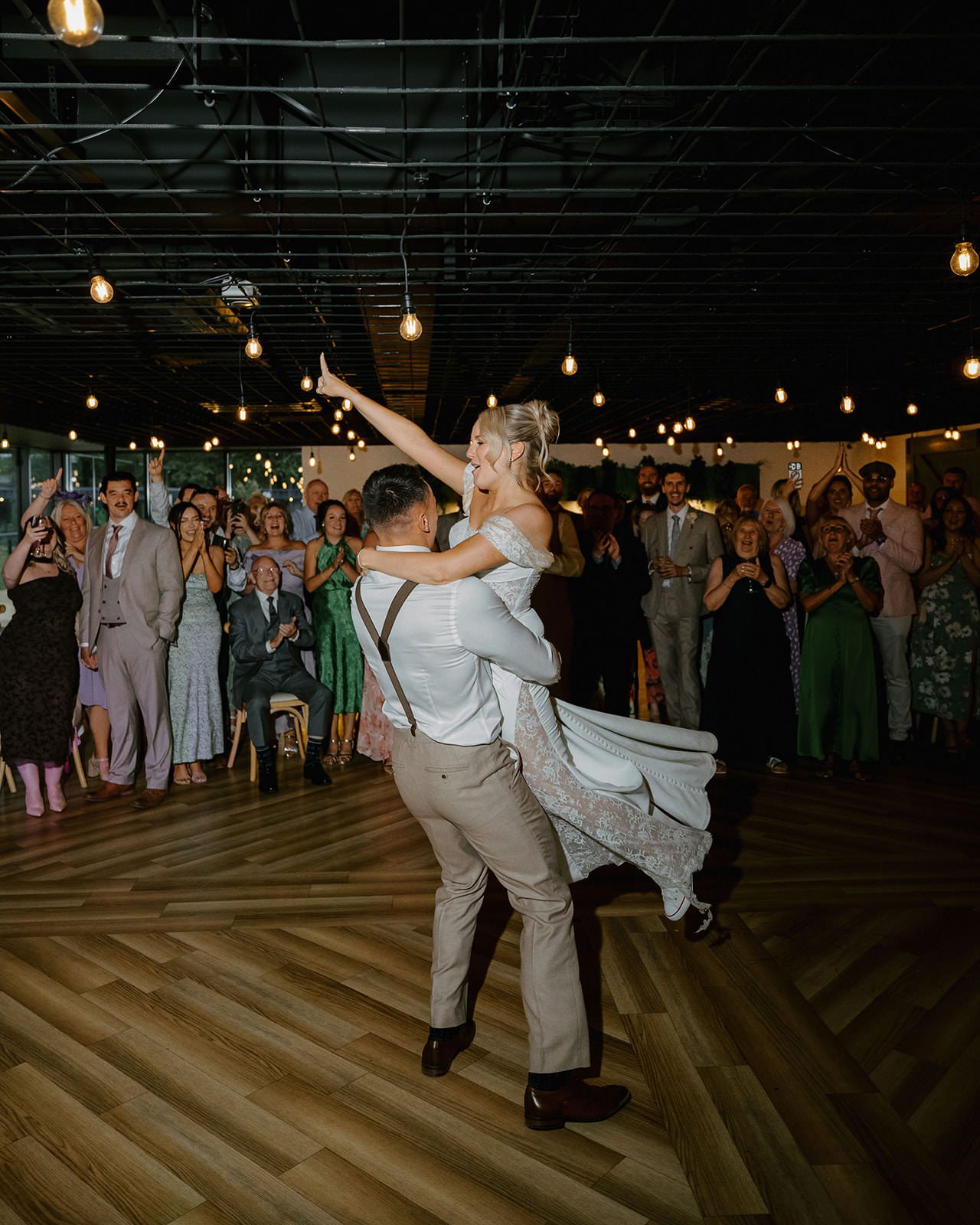 Groom lifting the bride into the air during their first dance as guests cheer