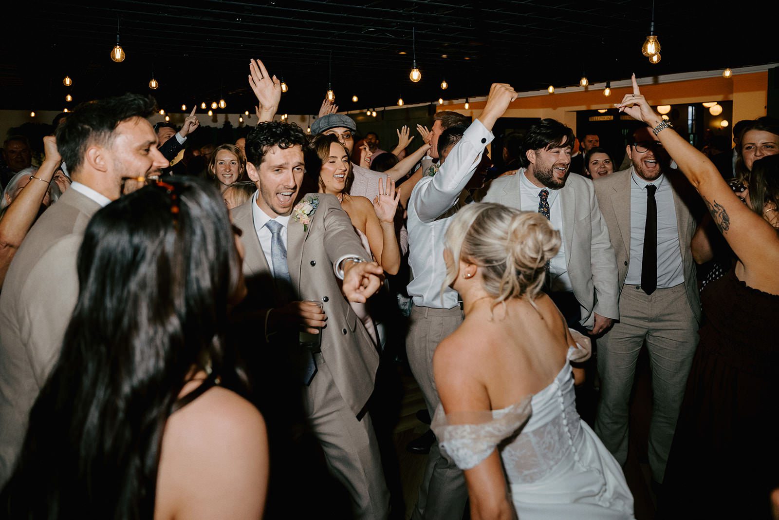 Bride and groom dancing with friends on a packed dance floor