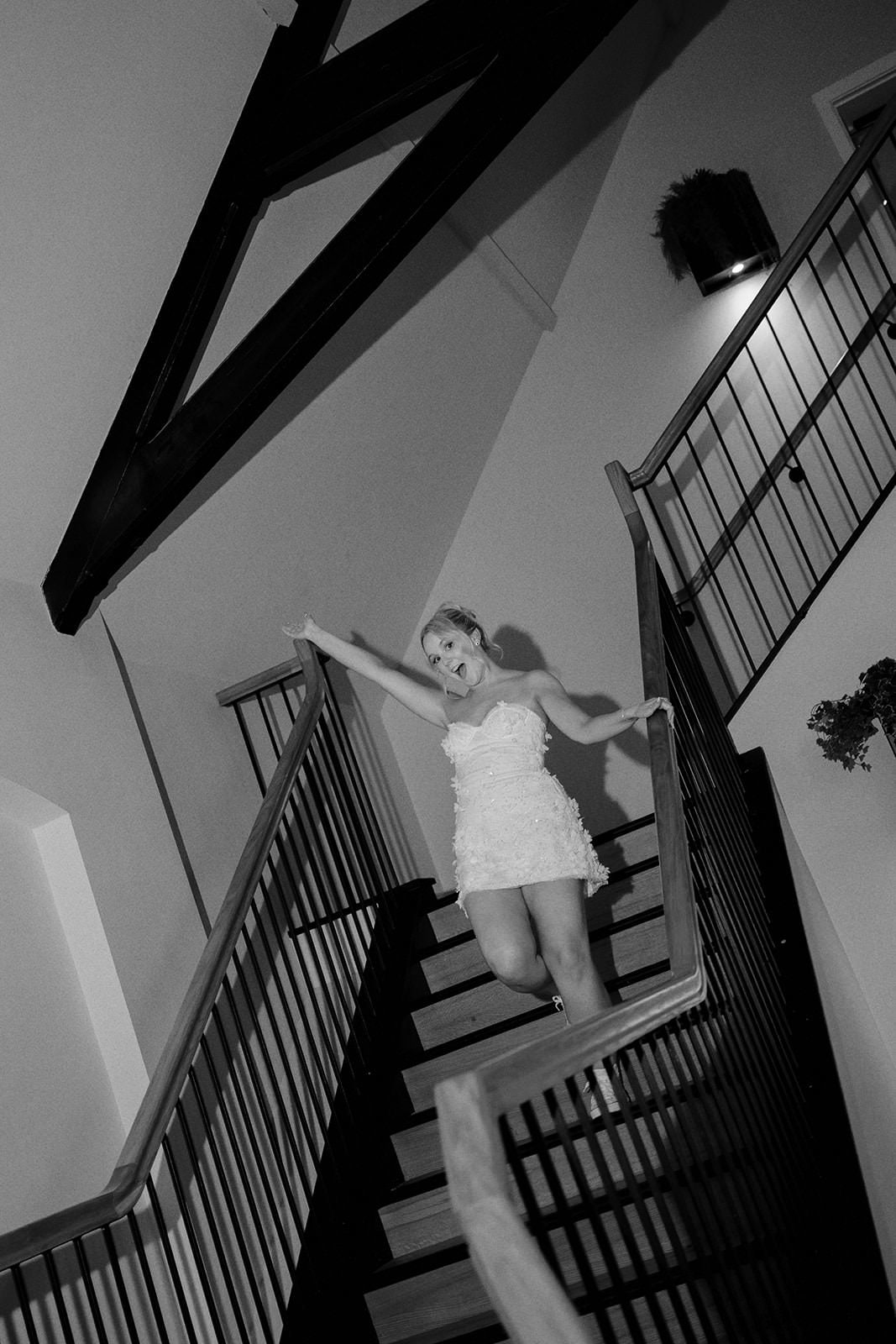 Black and white photo of the bride in a short party dress dancing down the staircase