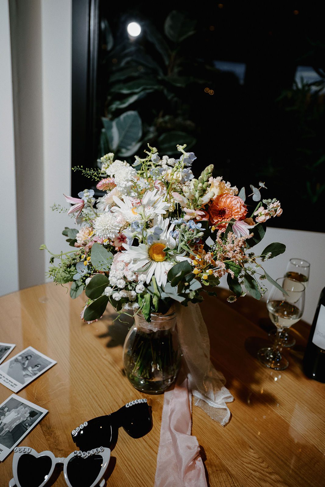 Wildflower bridal bouquet in a vase on a table with heart sunglasses and instant photos