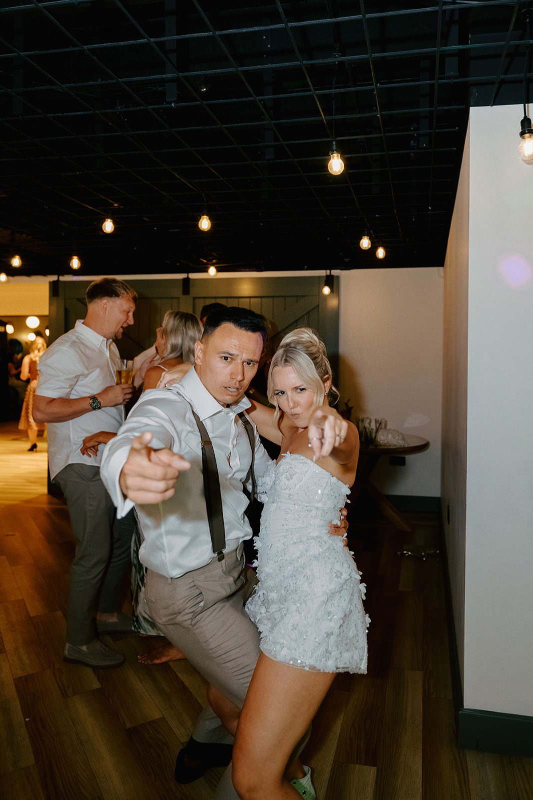 Bride and groom pointing at the camera while dancing in the evening