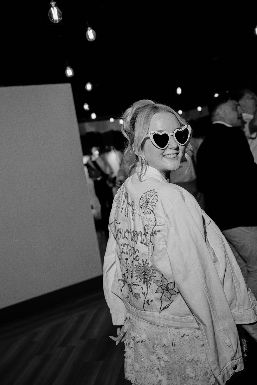 Black and white photo of the bride in heart sunglasses and a hand-painted personalised denim jacket