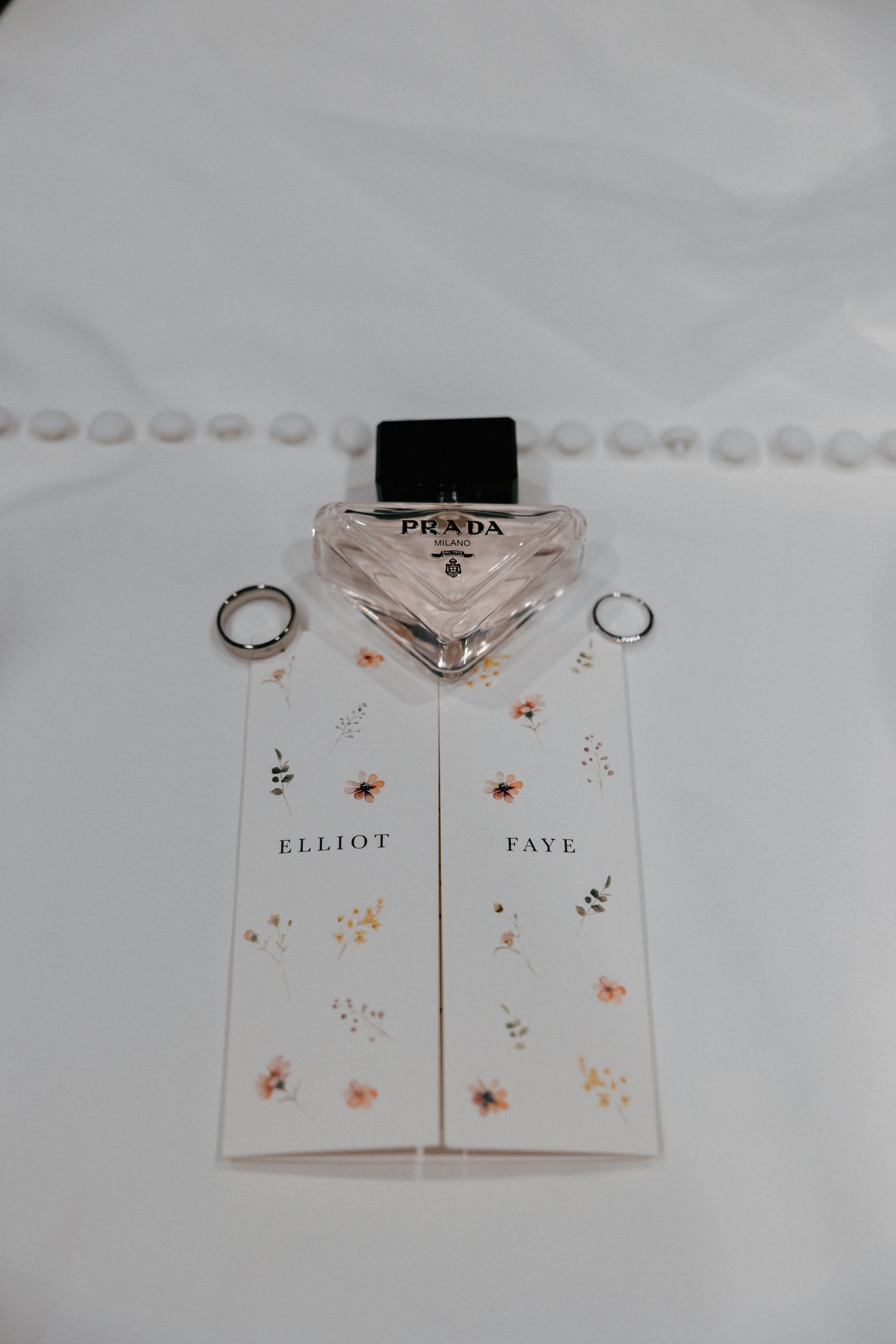 Perfume bottle and wedding rings resting on Elliot and Faye name cards on the bride's dress