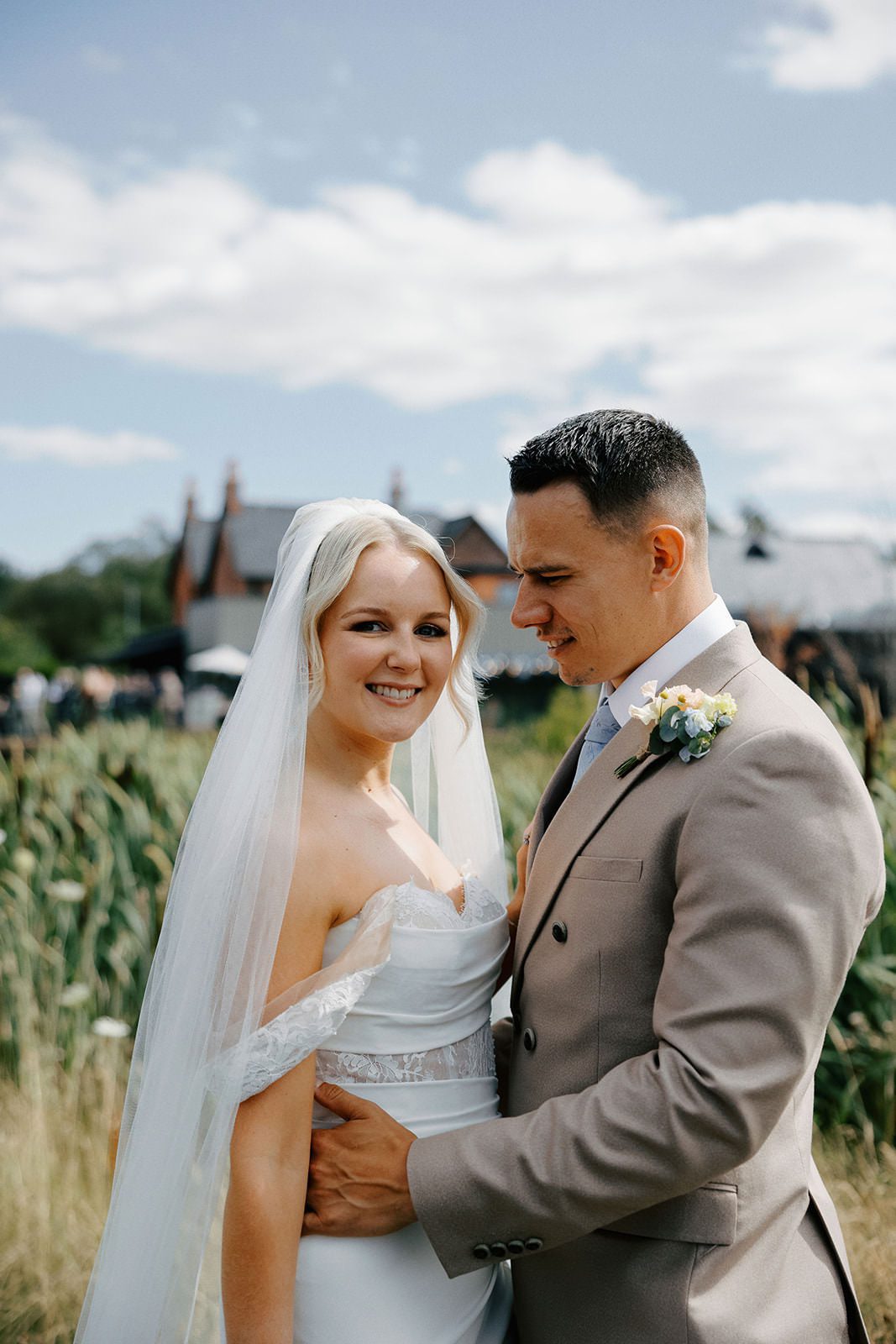 Bride smiling in her veil as the groom holds her, with the red-brick Whistle Barns buildings behind